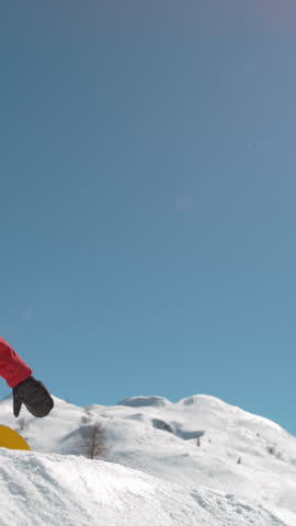 SLOW MOTION TIME WARP, LENS FLARE, BOTTOM UP: Snowflakes sparkle in the sunshine as male rider does snowboarding tricks. Fearless snowboarder does a spin trick while riding off a big air kicker.