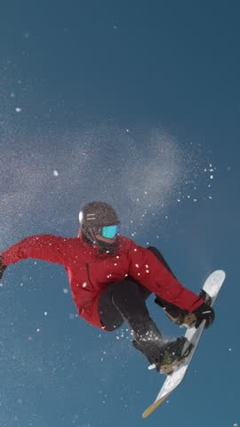 SLOW MOTION TIME WARP, LENS FLARE, BOTTOM UP: Snowflakes sparkle in the sunshine as male rider does snowboarding tricks. Fearless snowboarder does a spin trick while riding off a big air kicker.