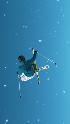 SLOW MOTION, CLOSE UP: Freestyle skier takes off a big kicker and does a spinning grab trick with crossed skis. Cinematic shot of a pro skier doing tricks on a sunny winter day in the Julian Alps.