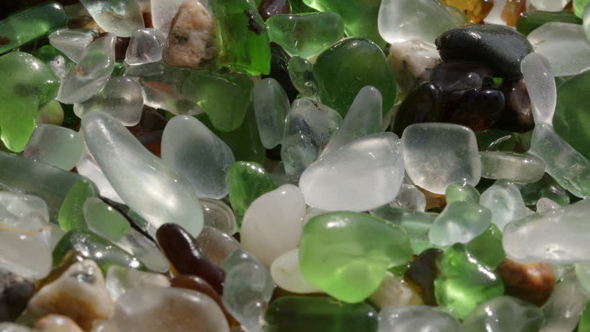 Camera panning right reveals wet sea glass and glistening rocks on a sunny beach, showcasing vibrant colors and textures. PLAYA DE LOS CRISTALES, Coruna, Spain