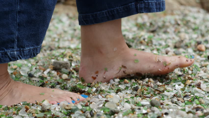 Woman walking carefully on a beach adorned with colorful sea glass, enjoying the beauty of nature and the ocean. PLAYA DE LOS CRISTALES, Coruna, Spain