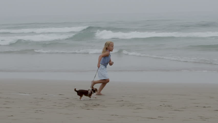 Young girl runs joyfully with her along a sandy beach, enjoying the sun and the playful ocean waves, filmed in slow motion