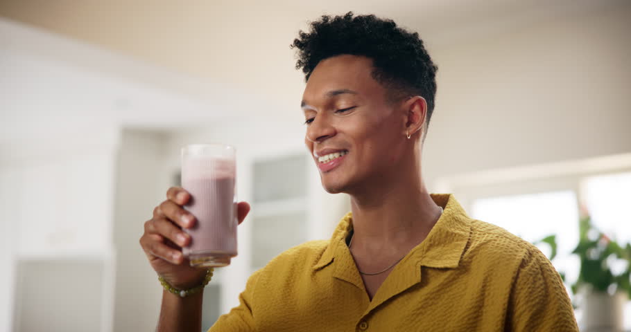 Home, man and happy with glass of smoothie in kitchen for diet, nutrition and healthy food. Apartment, male person and smile with milkshake or organic drink with vitamins and ingredient for wellness