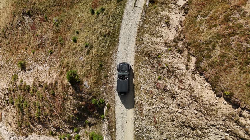 SUV driving down a narrow dirt road surrounded by dry, rugged landscape on a sunny day
