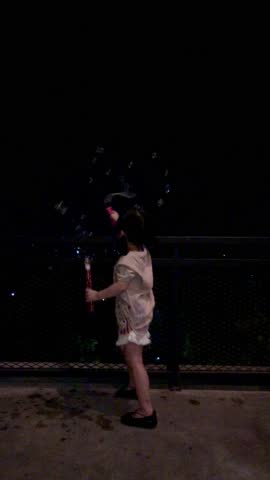 Beautiful Asian little girl wearing white t-shirt and shorts playing bubble gum in the garage at night