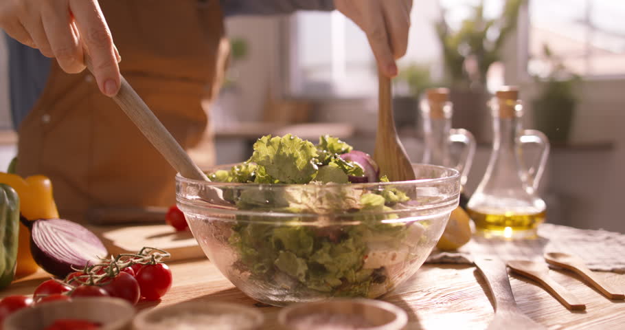 Closeup of a Fresh Mediterranean Salad Being Tossed and Mixed with Vibrant Vegetables in a Sunlit, Bright Kitchen