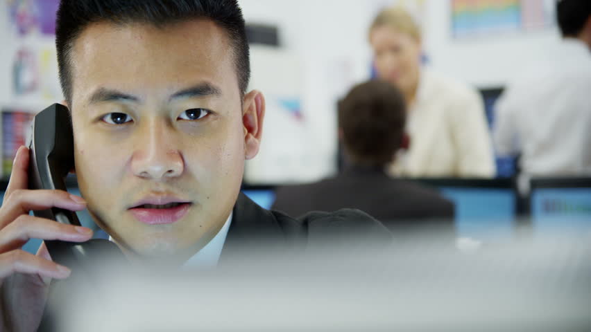 Young and ambitious stock market trader is doing a deal over the phone in a busy office filled with computers. The rest of his team are hard at work in the background.  Royalty-Free Stock Footage #3673151