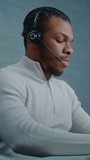 Vertical shot African American technical support specialist in headset works on computer, consults client via call, provides online customer service. Multiethnic team of hotline operators work. - Powered by Shutterstock - Get 15% off with code: PIKWIZARD15