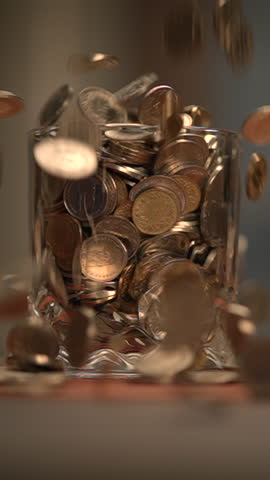 A beautiful sequence of shiny coins is falling gracefully into a glass jar container