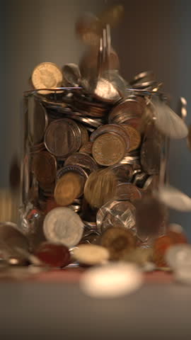 A beautiful sequence of shiny coins is falling gracefully into a glass jar container
