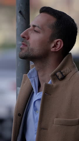 A Thoughtful and Contemplative Man is Smoking Outside While Wearing a Stylish Coat