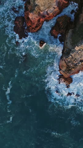 Aerial top view on Atlantic coast with rock cliffs and waves at sunset in Portugal. Vertical video