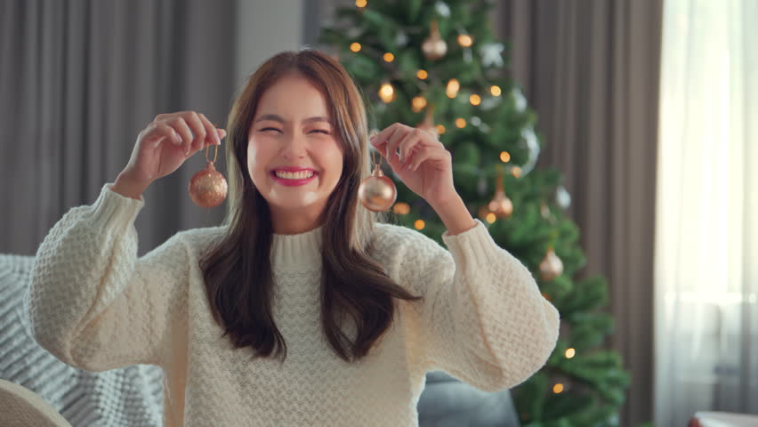 Happy asian woman celebrate winter holidays hold Christmas balls present decorate Christmas tree at home, Merry Christmas and Happy New Year!