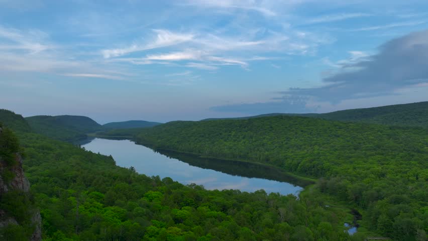 A breathtaking view of Lake of the Clouds at sunset during July, captured by drone footage in the Porcupine Mountains, Upper Peninsula, Michigan. The tranquil lake reflects the serene sky.