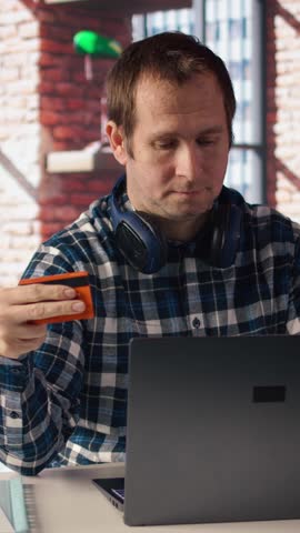 Happy man excited to do online shopping, typing debit card information on laptop in apartment. Cheerful person at desk using notebook, adding payment method on website, camera A