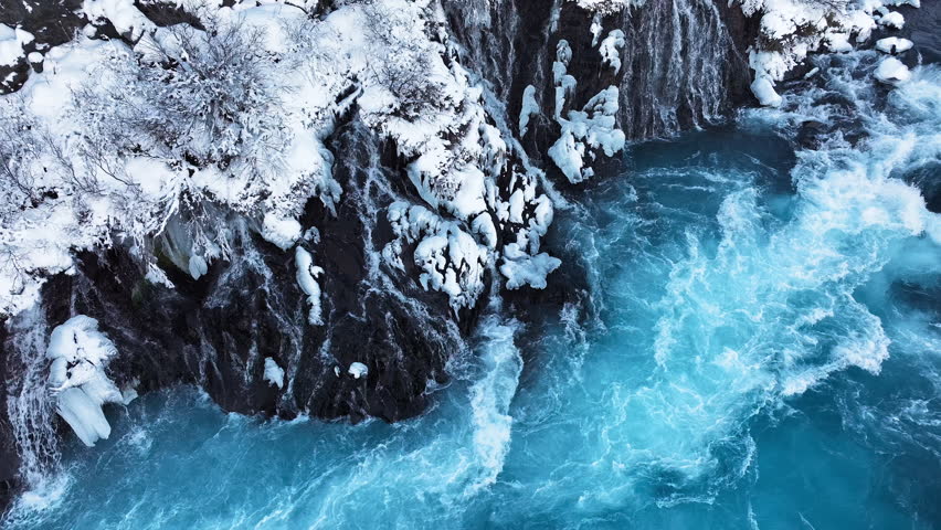 Incredible river with turquoise water, many small waterfalls flowing down from a volcanic hill covered with snow in winter. Frozen Icelandic landscape from a bird
