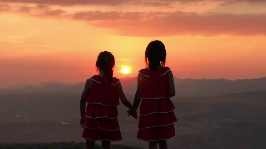 Silhouette of two little girls are happily playing on meadow during a summer sunset. Family love with colorful sunset.