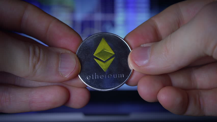 A Hand Holding an Ethereum Coin Set Against a Background of Digital Investment Strategy and Concepts
