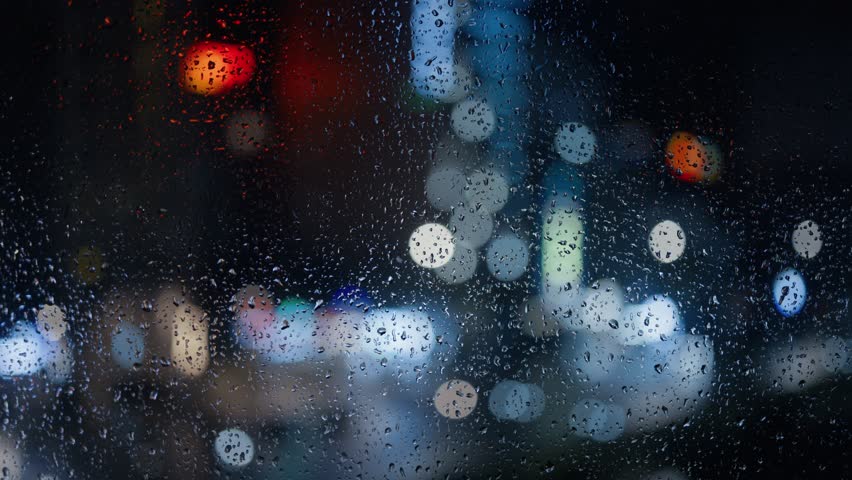 Raindrops on a window close-up against a blurred night city background.