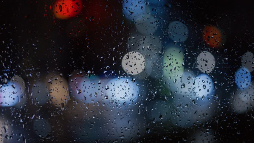 Raindrops on a window close-up against a blurred night city background.