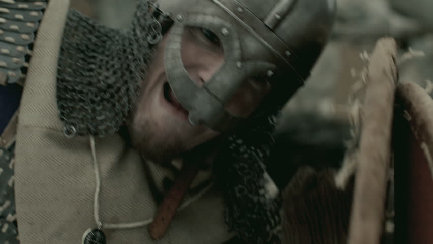 Brutal medieval warrior armored in chainmail and helmet, holding shield and stabbing enemy with sword in battle