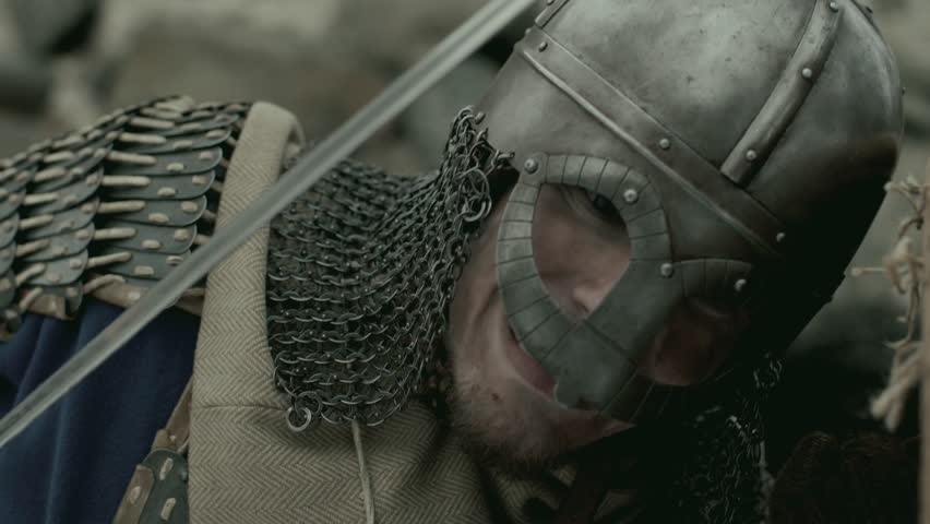 Brutal medieval warrior armored in chainmail and helmet, holding shield and stabbing enemy with sword in battle