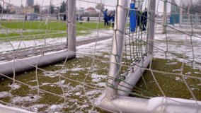 A snowcovered soccer training field with a completely visible goal and players visible in background - Powered by Shutterstock - Get 15% off with code: PIKWIZARD15