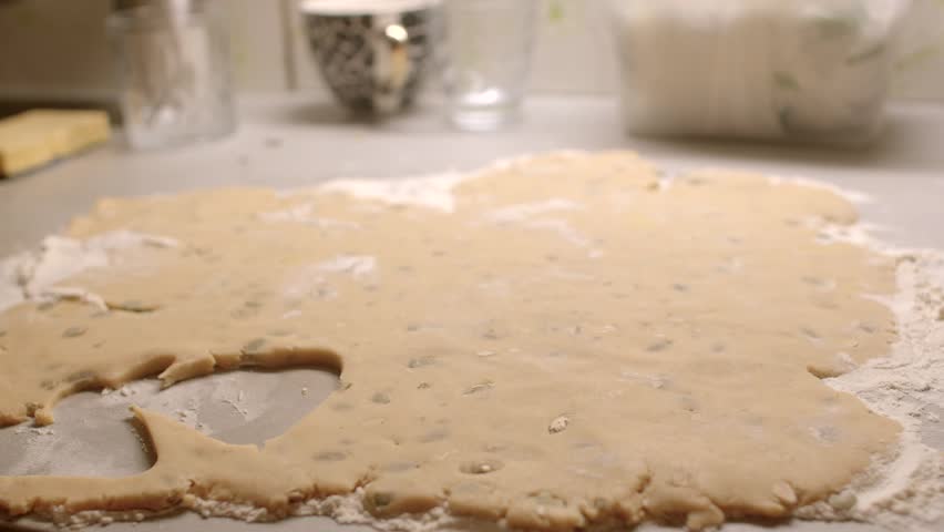 A hand skillfully cutting various shapes from rolledout cookie dough positioned on a floured surface
