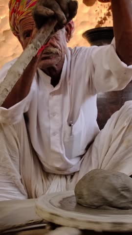 Skilled professional potter throwing the potter's wheel and shaping traditional ceramic vessel and clay ware: pot, jar in pottery workshop. Handwork craft from Shilpagram, Udaipur, Rajasthan, India