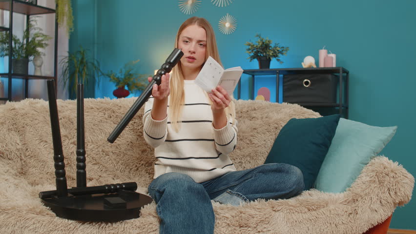 Caucasian woman girl tries to assemble small table from printed instructions sitting at home on sofa. Looks confused, worried, slightly frustrated, uncertain, holding a paper diagram, feeling unsure