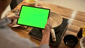 Senior man using digital tablet with a blank green screen while cooking in his home kitchen - Powered by Shutterstock - Get 15% off with code: PIKWIZARD15