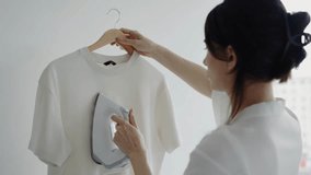 Close-up of a woman ironing a white t-shirt at home, creating a neat and wrinkle-free look. Woman Ironing Clothes at Home Near Large Window on an Overcast Day - Powered by Shutterstock - Get 15% off with code: PIKWIZARD15