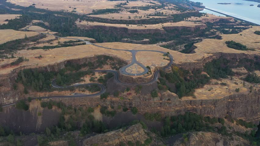 Aerial 4K drone footage of Rowena Crest in the Columbia River Gorge, Oregon, captured at sunrise. Features the iconic winding road, rugged cliffs, scenic views, and nearby parking areas with visitors 