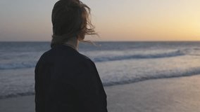 Blonde woman walking on the beach along the ocean at sunset. WomanWoman gazing at ocean waves  as the sun sets. Hair and dress flutter in the wind - Powered by Shutterstock - Get 15% off with code: PIKWIZARD15