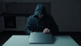 Unidentified man wearing a hood sitting in the kitchen, with a laptop. The image captures a moment of focused work, hinting at cyber activities. - Powered by Shutterstock - Get 15% off with code: PIKWIZARD15