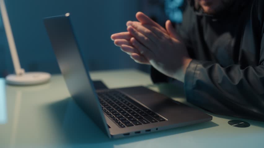 Hands of a male hacker typing on a laptop, engaged in online fraud, showing the physical aspect of cybercrime in a dark, secretive space.