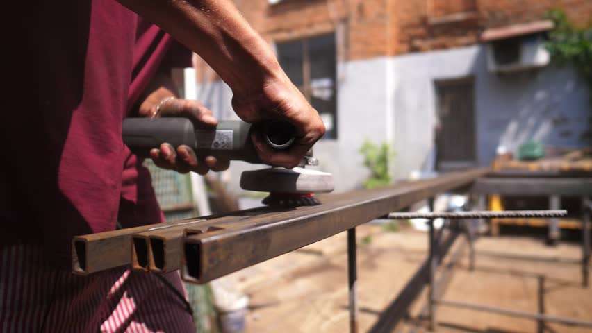 Male hands of professional mechanic holding special instrument and clearing metal construction from rust outdoor. Arms of young worker grinding iron detail with electric circular saw tool. Close up