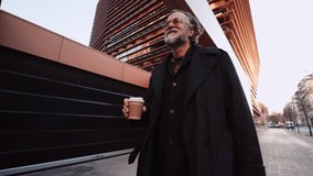 Happy Mature man with joyful expression enjoys his morning coffee while walk near office building. 60 years old male gazes upward, exuding contentment and sense of peace in city moving confidently - Powered by Shutterstock - Get 15% off with code: PIKWIZARD15