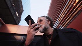 60 years old man records voice message on smartphone, surrounded by sleek modern architecture. low-angle view, integration of technology into everyday life communication.Sending audio to colleague - Powered by Shutterstock - Get 15% off with code: PIKWIZARD15