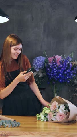 The female florist in flower shop takes a photo of the result of the work and sends it to the client before delivery. vertical video