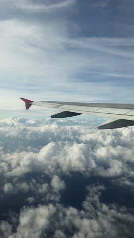 View from the airplane window to the clouds, the plane flies over the sea. Vertically footage.