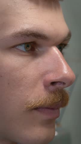 Man is brushing teeth with toothbrush in modern bathroom in the morning, close up of face. Male brushes his teeth with toothpaste, doing morning oral anticavity hygiene routine. Vertical video
