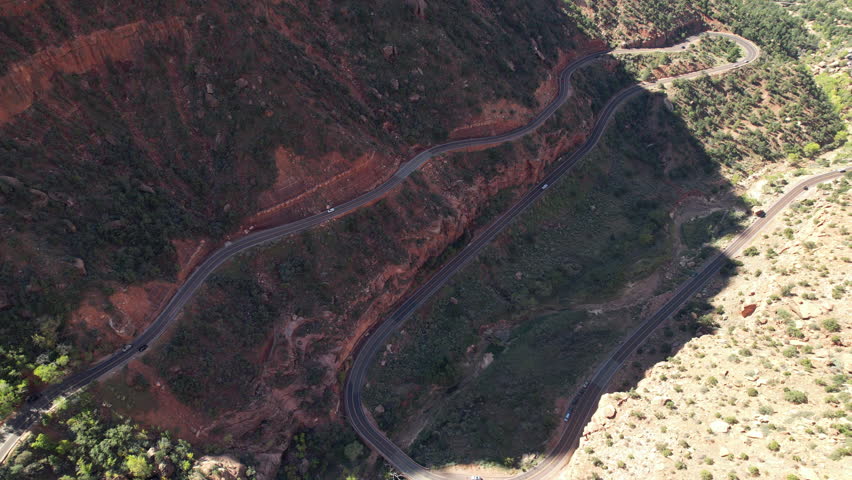 A stunning aerial perspective of a winding road carved into the red rock cliffs of Zion National Park. The road twists and turns, offering breathtaking views of the rugged terrain.