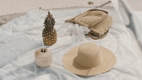 A stylish beach setting with a straw hat, fresh pineapple, coconut drink, and woven bag arranged on white fabric in the sand. Ideal for tropical vacation, summer, and lifestyle themes.  - Powered by Shutterstock - Get 15% off with code: PIKWIZARD15