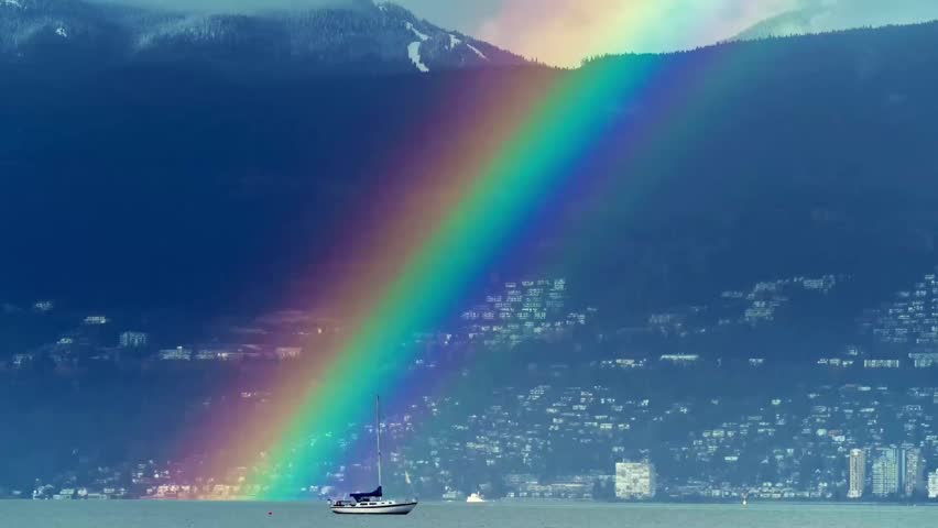 The image features a stunning rainbow stretching across a mountainous landscape, touching down near a body of water where a boat is anchored. The vibrant colors of the rainbow contrast beautifully wit