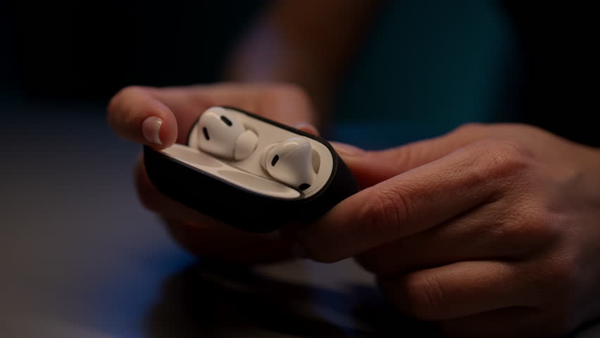 Close-up of young woman holding sleek black case with white wireless earbuds for music or calls on go, showcasing modern technology seamlessly integrated into daily life. Shooting in slow motion.