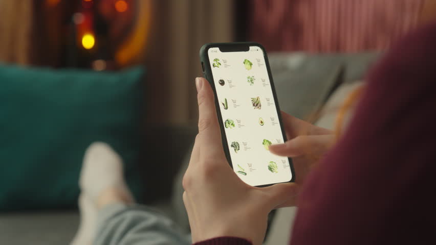 Back view unrecognizable woman girl female shopper buyer browsing mobile phone screen internet store order online shopping at home choose vegetables buy products supermarket delivery cellphone website