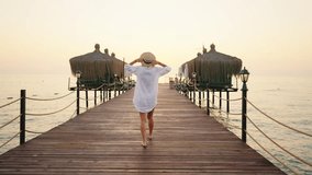 Slender blonde woman in white cotton shirt walking alone on wooden pier. Beautiful sunset or sunrise and female person in marina, back view, following shot, slow motion, carefree lady traveler - Powered by Shutterstock - Get 15% off with code: PIKWIZARD15