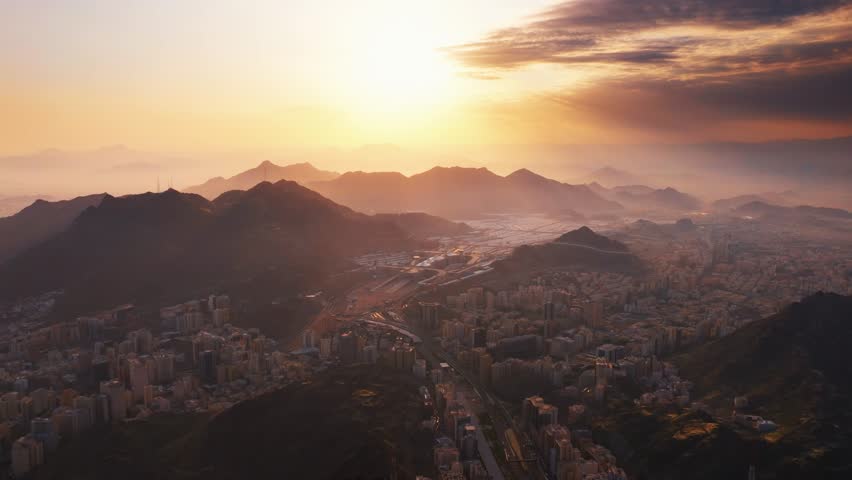 Mecca, Saudi Arabia - A breathtaking aerial view of Mecca city at sunrise, showing urban architecture surrounded by majestic mountains under a golden sky