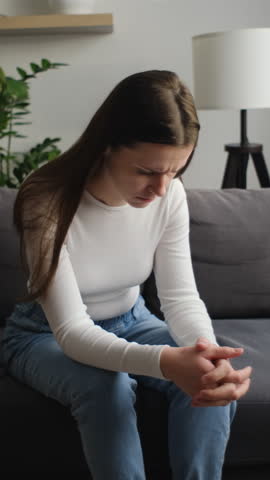 Vertical footage of worried young caucasian woman sitting on couch alone, upset desperate female thinking about life, health or emotional problem, feeling sad, suffering from anxiety concept